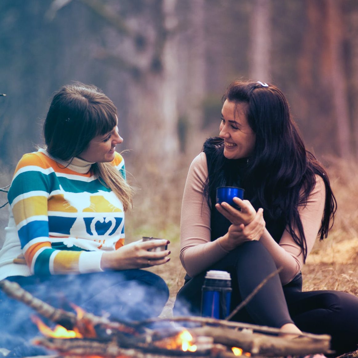 two women sitting on ground near bonfire